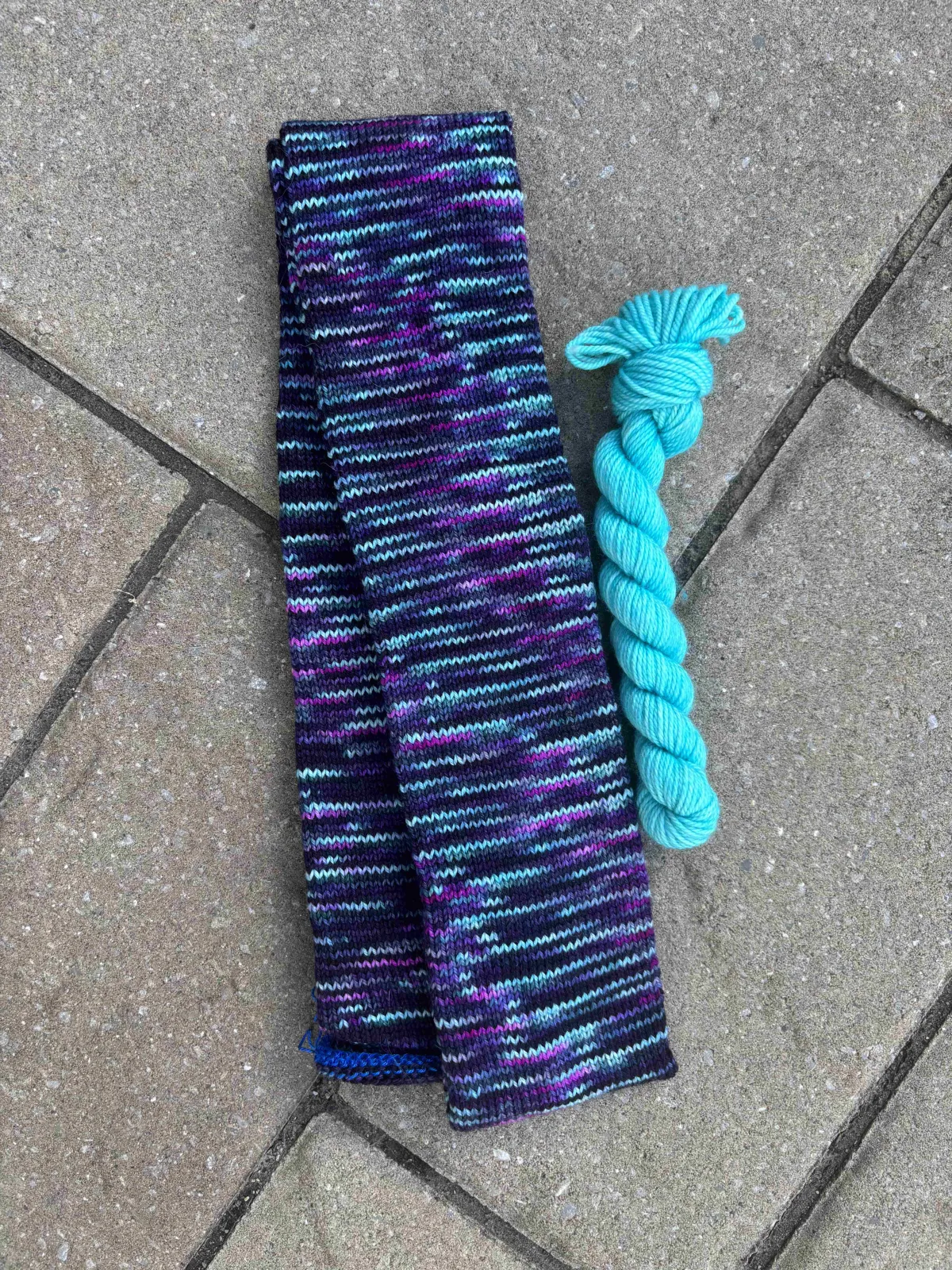 Knitted sock tube in blues and purples with accompanying bright blue mini skein
